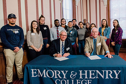 President Jake Schrum signs documents with Paul L. Phillips '64 surrounded by students from the Bonner Scholars Program.