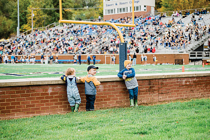 Homecoming 2021: Children standing near a low wall enjoying the football game.