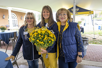 A group of alumni with the individual in the middle holding a bouquet of flowers