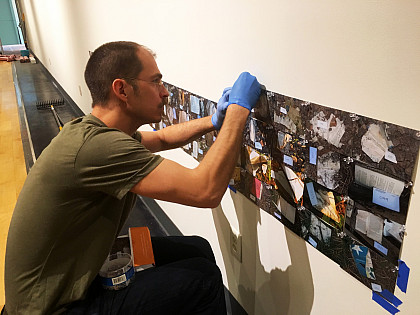 Artist Micah Bloom works to hang hundreds of photographs in his installation of Codex, a site specific installation in the MCA Art Gallery