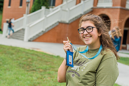 First-year student posing with their room key in front of the dorms.