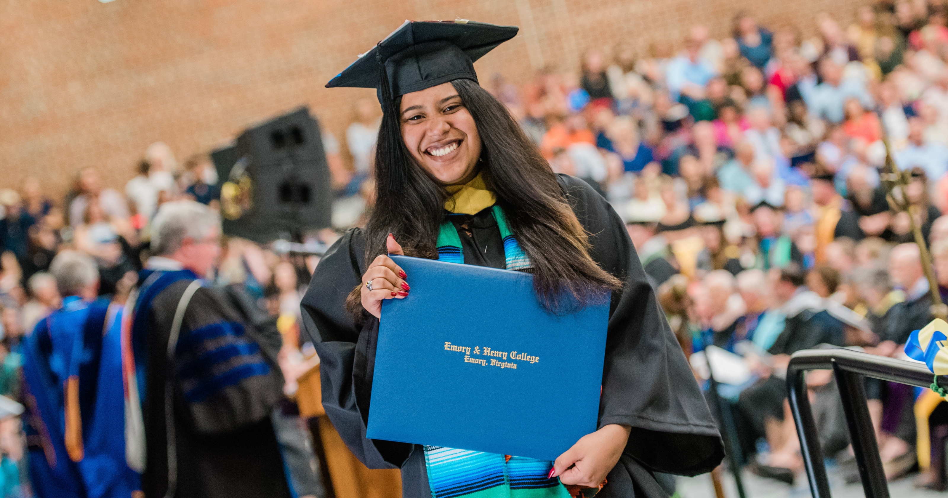 A student walks across the stage with her diploma at graduation.